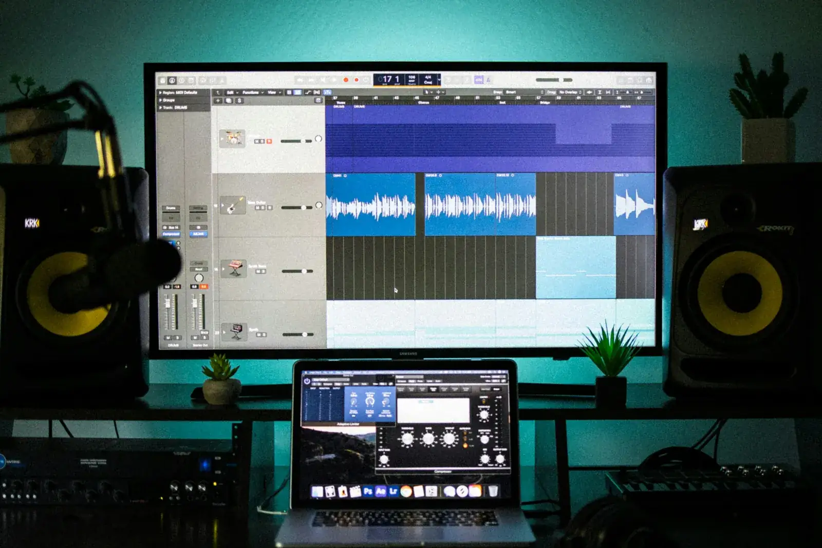 A home studio desk with music production software on a monitor and a laptop