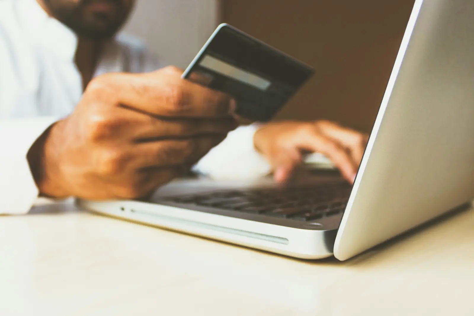 A hand holding a credit card at a laptop