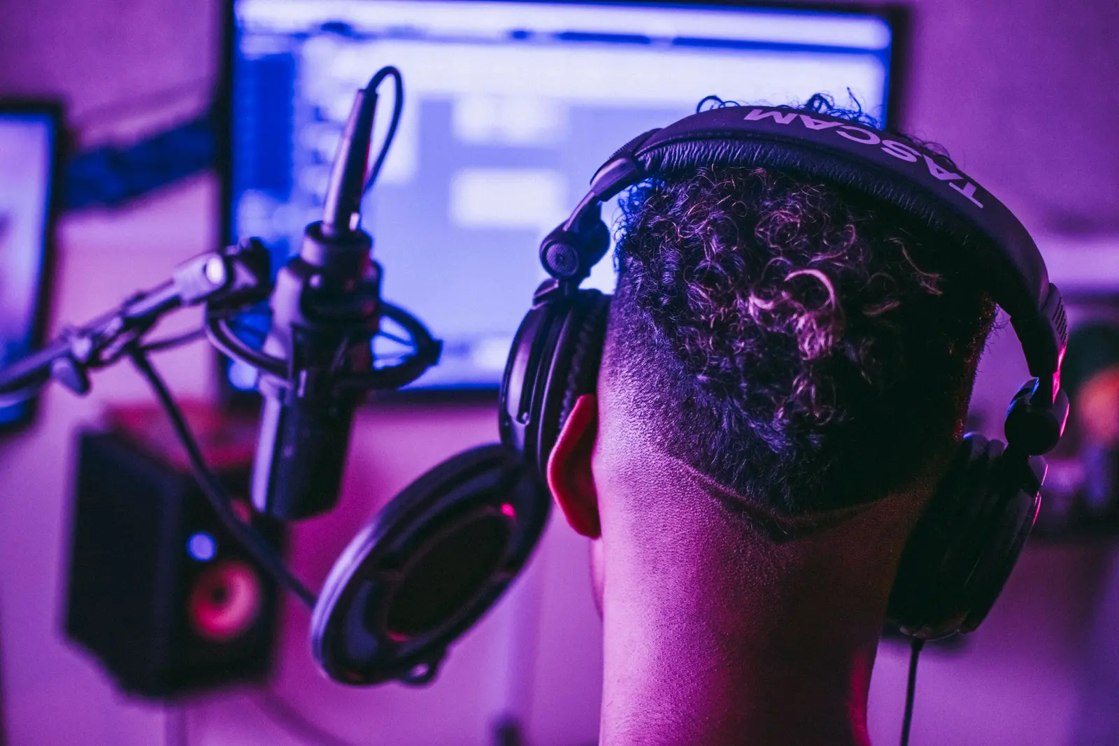 The back of a head wearing studio headphones in front of a microphone
