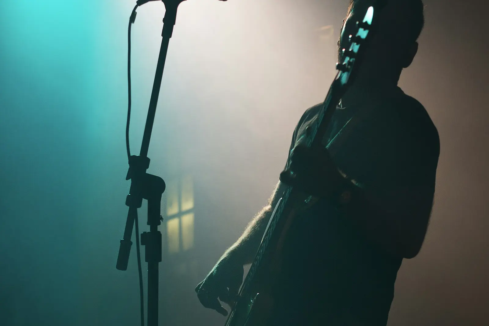 A singer with a guitar on a stage lit in teal